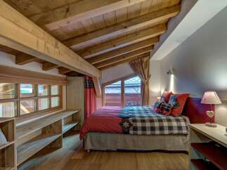 Experience cozy mountain living in this charming bedroom featuring a rustic wooden ceiling with exposed beams and a comfortable bed adorned with plaid bedding.