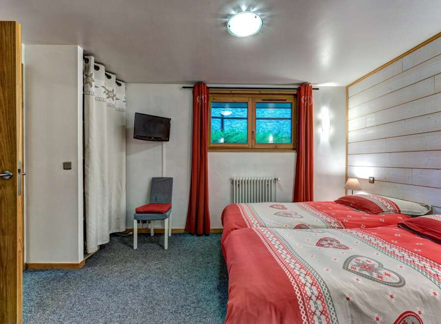 This charming bedroom features two comfortable twin beds adorned with festive red and white heart-patterned duvets, perfect for a cozy mountain getaway.