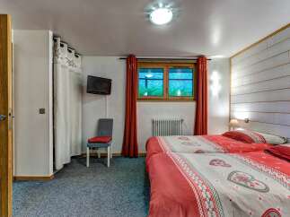 This charming bedroom features two comfortable twin beds adorned with festive red and white heart-patterned duvets, perfect for a cozy mountain getaway.
