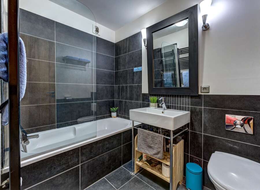 This modern bathroom features a sleek design with dark tiled walls and a clean white bathtub.