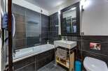 This modern bathroom features a sleek design with dark tiled walls and a clean white bathtub.