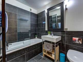 This modern bathroom features a sleek design with dark tiled walls and a clean white bathtub.