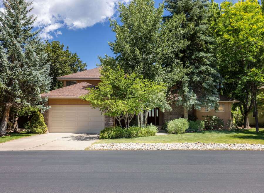 Discover this charming home featuring a spacious two-car garage and a welcoming front entrance surrounded by mature trees and lush landscaping.