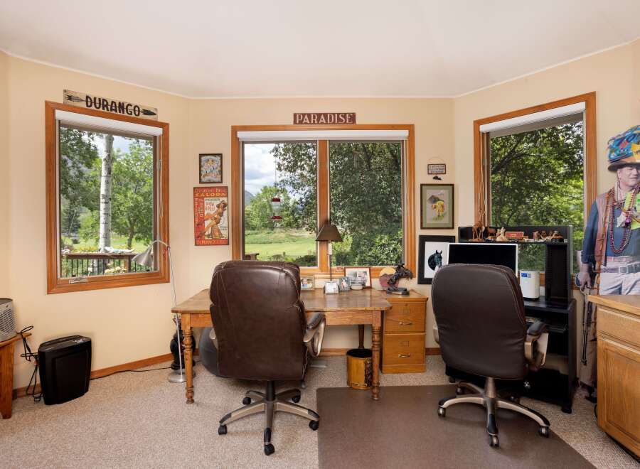 This home office offers a productive and inspiring workspace with large windows overlooking a lush green landscape.