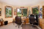 This home office offers a productive and inspiring workspace with large windows overlooking a lush green landscape.