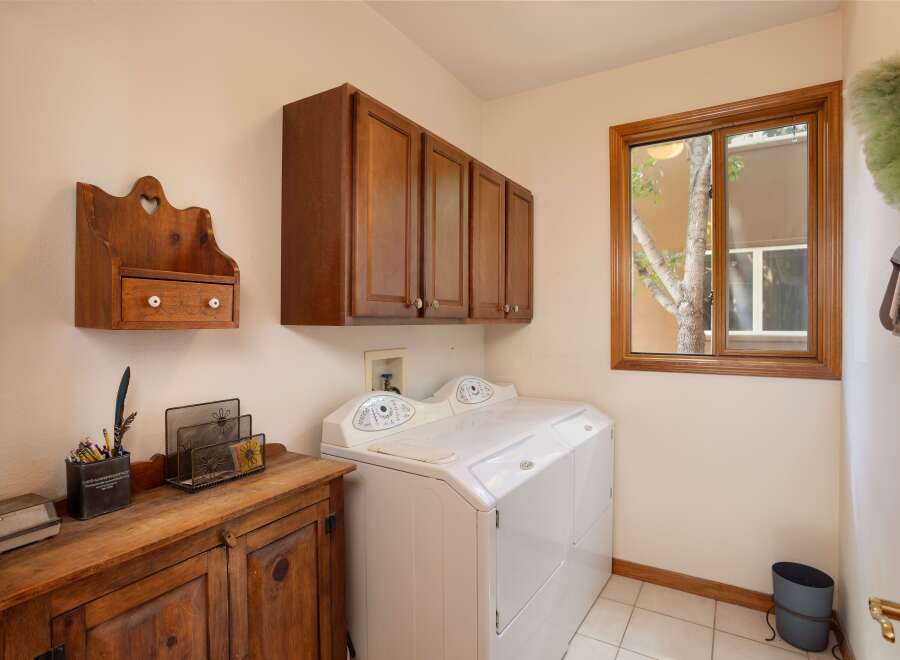 This laundry room features a white top-loading washing machine and dryer set, complemented by dark wood upper cabinets for ample storage.