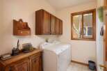 This laundry room features a white top-loading washing machine and dryer set, complemented by dark wood upper cabinets for ample storage.