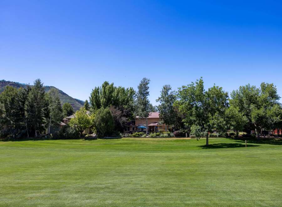 Experience luxury living with this stunning property, featuring a sprawling green lawn perfect for outdoor activities and a backdrop of lush trees and majestic mountains.
