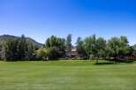 Experience luxury living with this stunning property, featuring a sprawling green lawn perfect for outdoor activities and a backdrop of lush trees and majestic mountains.