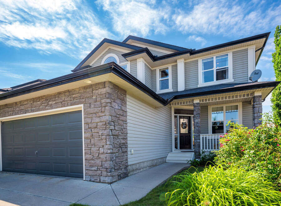 This stunning two-story home features a modern gray garage door and a welcoming front porch with stone accents.