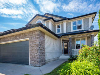 This stunning two-story home features a modern gray garage door and a welcoming front porch with stone accents.