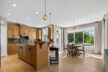 This spacious kitchen and dining area boasts beautiful natural light streaming through large windows, highlighting the warm wood cabinetry and elegant pendant lighting.