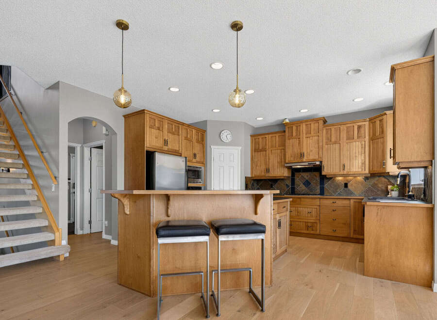 This spacious kitchen boasts beautiful natural wood cabinetry, a large island with seating, and a sleek stainless steel refrigerator.