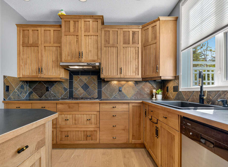 This spacious kitchen boasts beautiful natural wood cabinetry with intricate detailing, complemented by a striking slate tile backsplash.