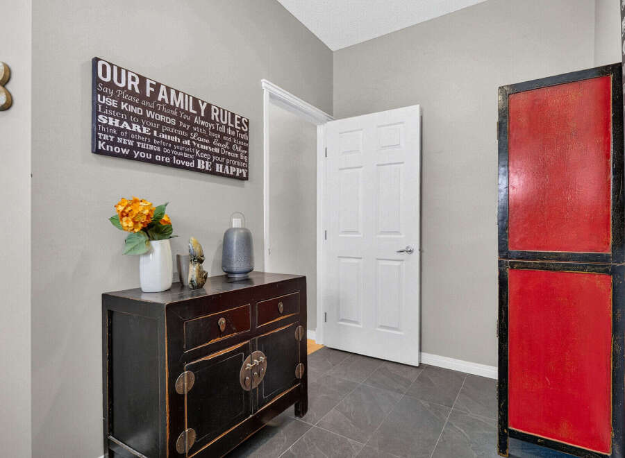 Welcome guests into a warm and inviting entryway featuring a charming 'Our Family Rules' sign, a decorative black cabinet with floral accents, and a striking red and black accent cabinet.