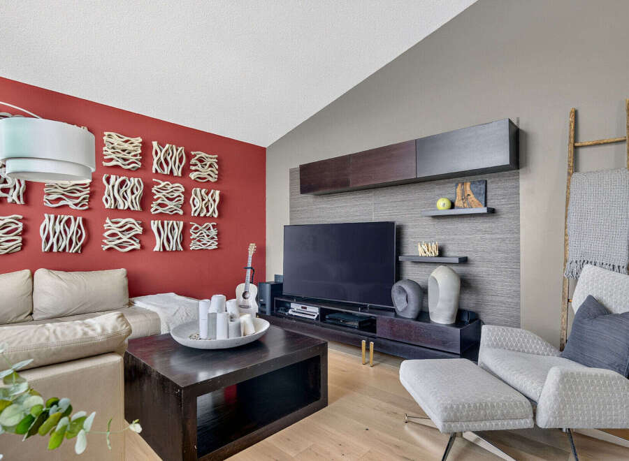 This modern living room features a striking red accent wall adorned with unique textured art pieces, complemented by a plush beige sectional sofa.