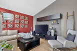 This modern living room features a striking red accent wall adorned with unique textured art pieces, complemented by a plush beige sectional sofa.