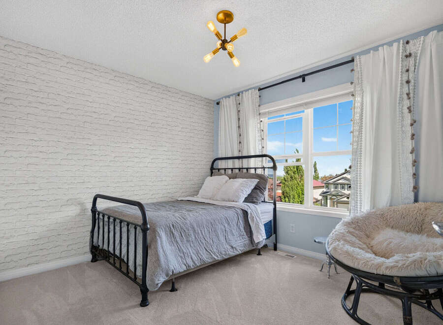This charming bedroom features a stylish black metal bed with a grey comforter and white pillows, complemented by a unique white brick accent wall.