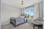 This charming bedroom features a stylish black metal bed with a grey comforter and white pillows, complemented by a unique white brick accent wall.