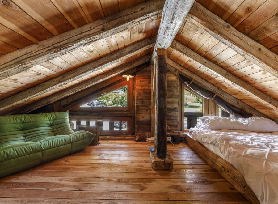 Experience rustic charm in this unique attic loft bedroom, featuring exposed wooden beams and a cozy green sofa.