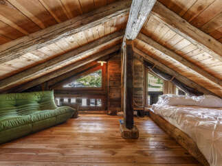Experience rustic charm in this unique attic loft bedroom, featuring exposed wooden beams and a cozy green sofa.