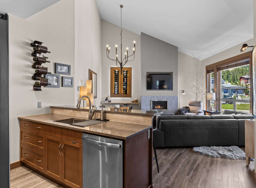 Experience luxury mountain living in this stunning property featuring a modern kitchen with a wine rack and a spacious living area with a fireplace and large windows offering breathtaking views.