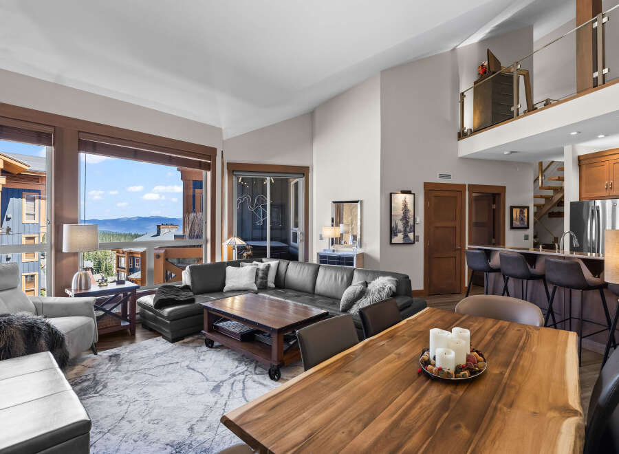 Experience luxurious mountain living in this stunning open-concept living space, featuring a large sectional sofa and a rustic wooden dining table perfect for gatherings.