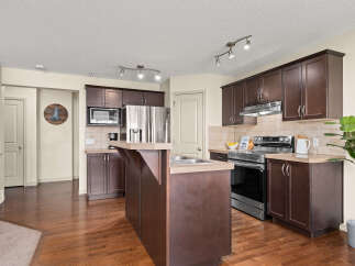 This spacious kitchen features dark wood cabinetry, stainless steel appliances, and a large island with a sink, perfect for meal preparation and entertaining.