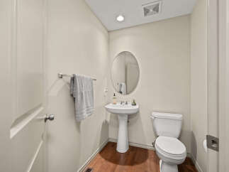 This powder room features a white pedestal sink with a chrome faucet and an oval mirror above.
