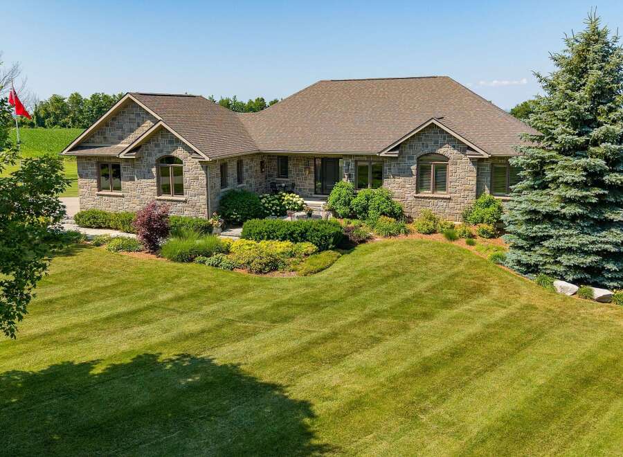 Discover this stunning stone-clad residence, featuring a beautifully landscaped yard with vibrant greenery and mature trees.
