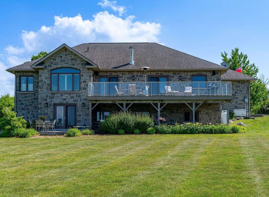 This stunning stone-clad home features a spacious walk-out basement and an expansive upper-level deck with glass railings, perfect for entertaining.