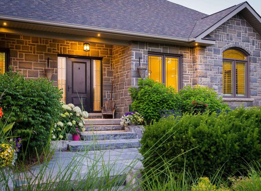 Step into luxury with this stunning stone-clad home, featuring a grand entrance with a dark wood door and elegant sidelights.