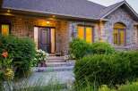Step into luxury with this stunning stone-clad home, featuring a grand entrance with a dark wood door and elegant sidelights.