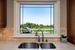 Enjoy picturesque views from this kitchen window, overlooking a lush green landscape and a clear blue sky.