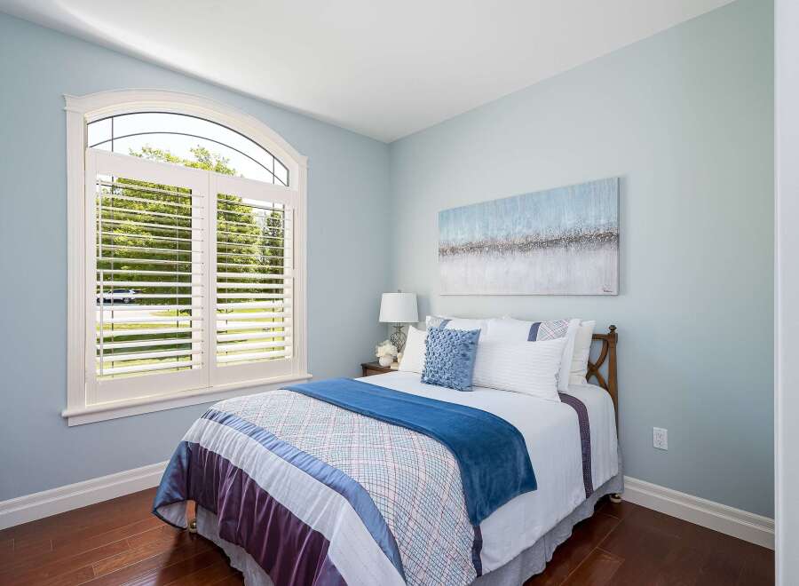 This inviting bedroom features a large arched window with white plantation shutters, flooding the space with natural light.