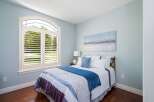 This inviting bedroom features a large arched window with white plantation shutters, flooding the space with natural light.