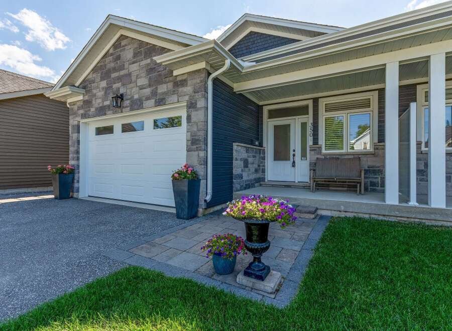 This charming home features a modern facade with a mix of stone and dark siding, complemented by a pristine white garage door and a welcoming covered porch.