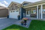 This charming home features a modern facade with a mix of stone and dark siding, complemented by a pristine white garage door and a welcoming covered porch.