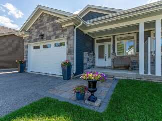 This charming home features a modern facade with a mix of stone and dark siding, complemented by a pristine white garage door and a welcoming covered porch.