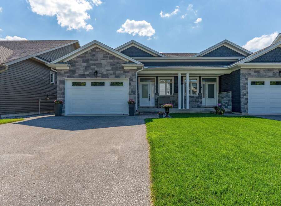 Discover this stunning modern home featuring a striking stone and dark siding facade, complemented by a well-maintained lawn and a spacious driveway.