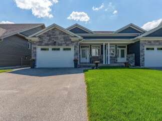 Discover this stunning modern home featuring a striking stone and dark siding facade, complemented by a well-maintained lawn and a spacious driveway.