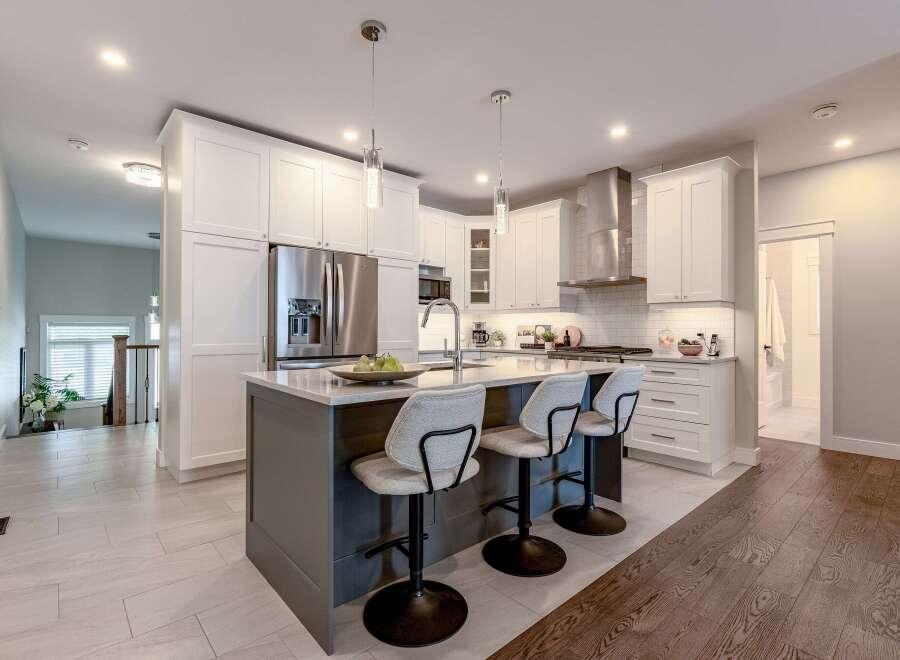 Experience modern luxury in this stunning kitchen, featuring sleek white cabinetry, a spacious island with seating, and top-of-the-line stainless steel appliances.