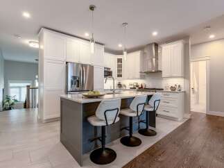 Experience modern luxury in this stunning kitchen, featuring sleek white cabinetry, a spacious island with seating, and top-of-the-line stainless steel appliances.