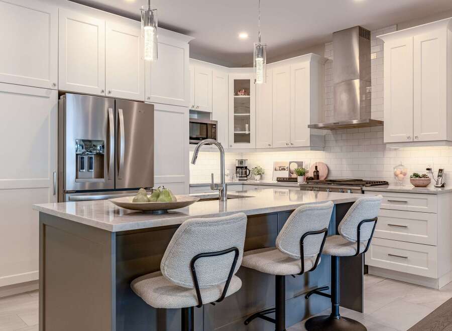 Experience modern luxury in this stunning kitchen, featuring sleek white cabinetry, a spacious island with a waterfall countertop, and top-of-the-line stainless steel appliances.