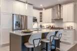 Experience modern luxury in this stunning kitchen, featuring sleek white cabinetry, a spacious island with a waterfall countertop, and top-of-the-line stainless steel appliances.