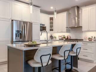 Experience modern luxury in this stunning kitchen, featuring sleek white cabinetry, a spacious island with a waterfall countertop, and top-of-the-line stainless steel appliances.