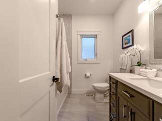 This modern bathroom features a sleek vanity with a white countertop and dark wood cabinets, complemented by a large, mosaic-tiled mirror.