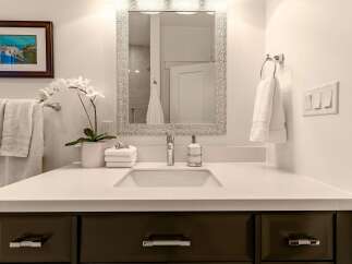 This modern bathroom vanity features a sleek white countertop with an undermount sink, complemented by a chrome faucet and a stylish soap dispenser.