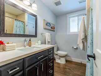 This beautifully updated bathroom features a dark wood vanity with a quartz countertop, complemented by a modern chrome faucet and a large framed mirror.