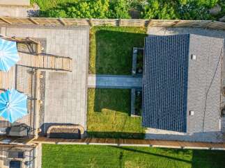 Experience outdoor living at its finest with this beautifully landscaped backyard, featuring a spacious wooden deck perfect for entertaining and two large blue umbrellas providing ample shade.